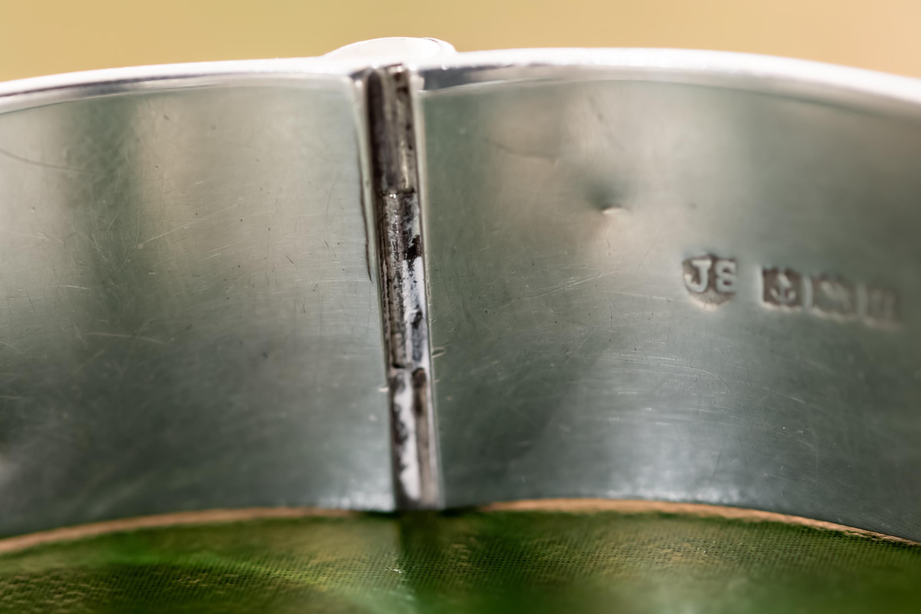 Close-up of a wide, vintage 1969 Birmingham sterling silver hinged bangle with intricate botanical engravings and a safety chain, resting beautifully on a vintage leather-bound book.