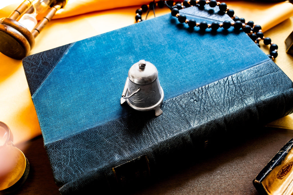 Miniature antique silver pail with a small handle, sitting on top of a dark blue vintage book.
