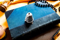 Miniature antique silver pail with a small handle, sitting on top of a dark blue vintage book.
