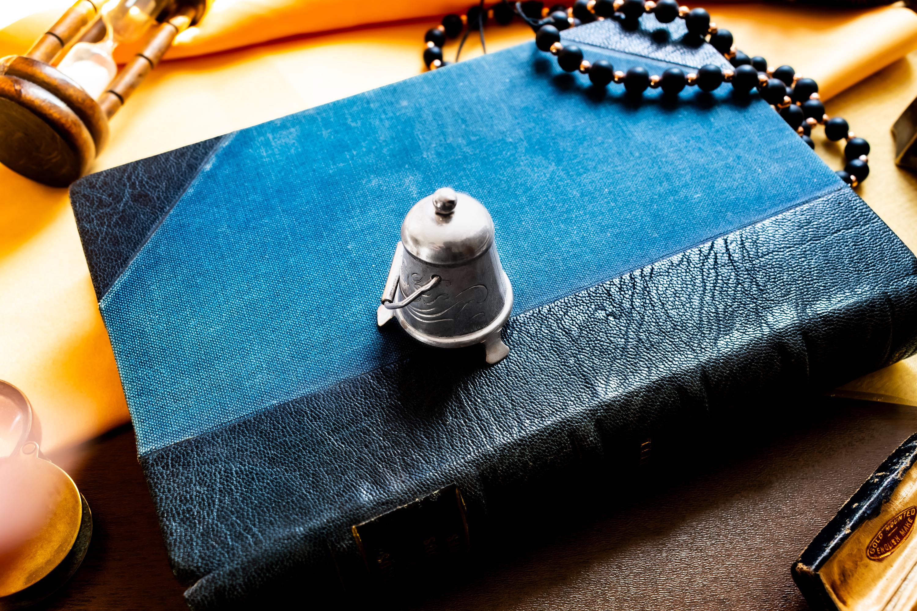Miniature antique silver pail with a small handle, sitting on top of a dark blue vintage book.