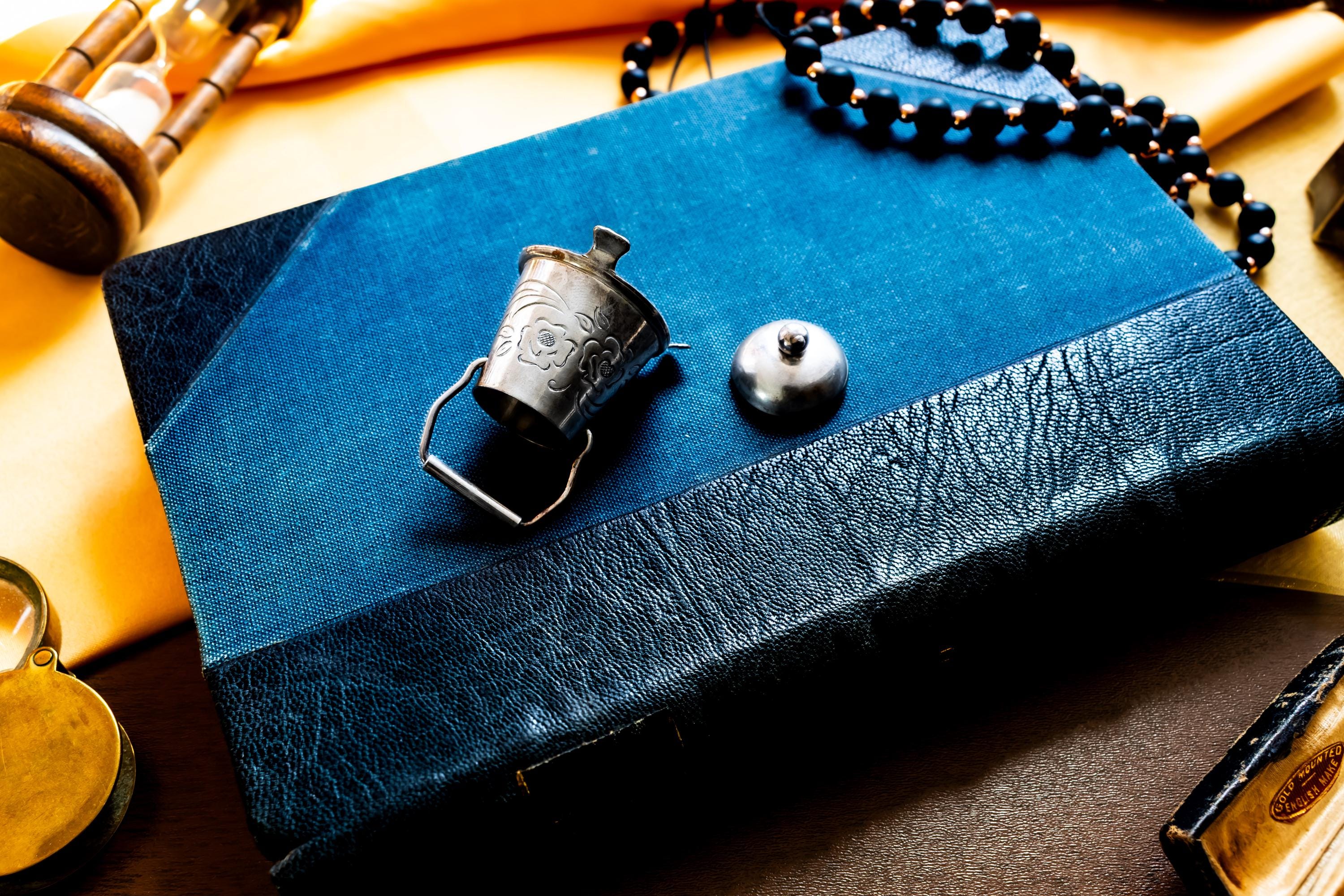 A image showing the side of a Miniature antique silver pail with a small handle, sitting on top of a dark blue vintage book.