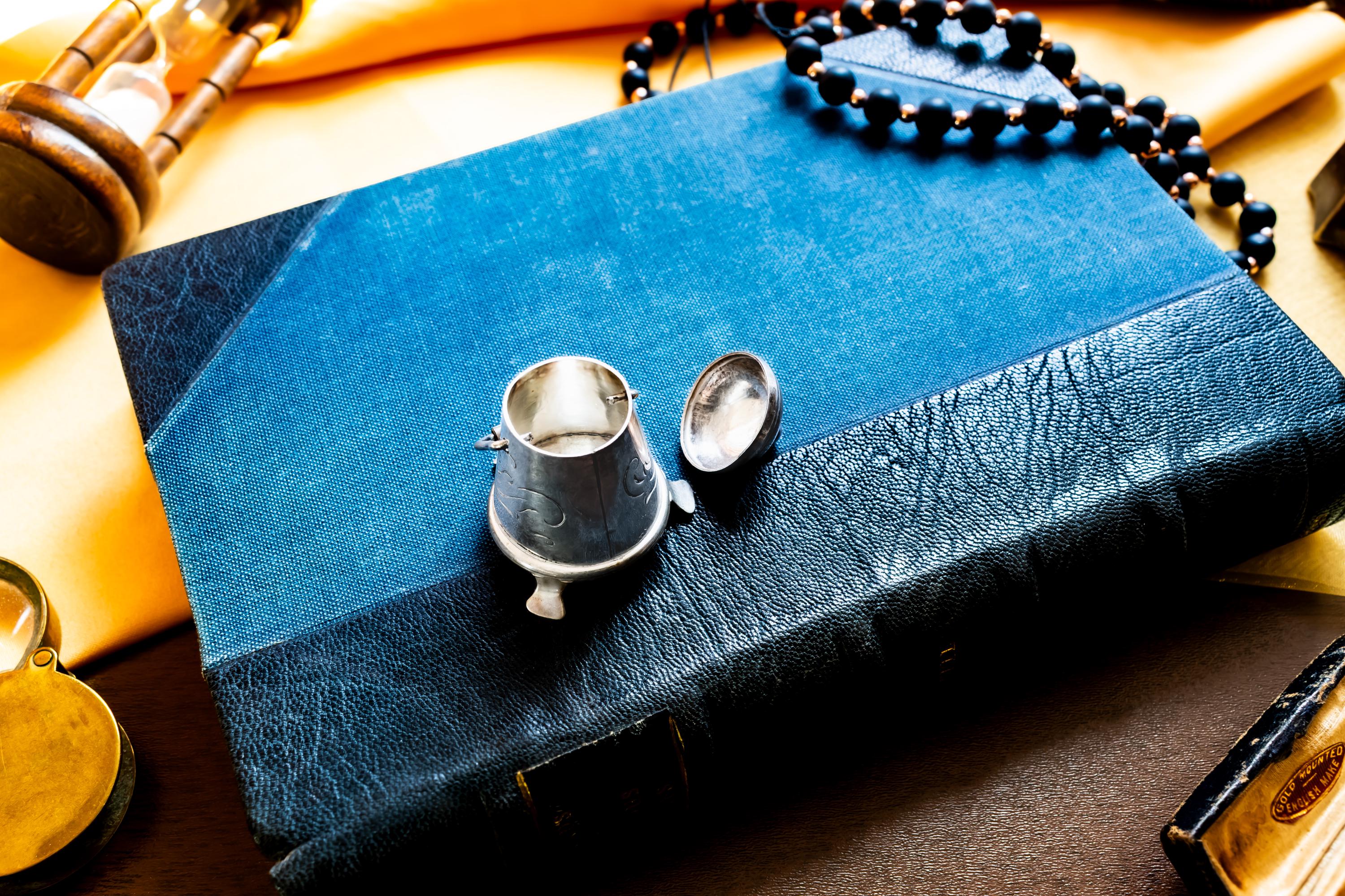 Miniature antique silver pail with a small handle, sitting on top of a dark blue vintage book.