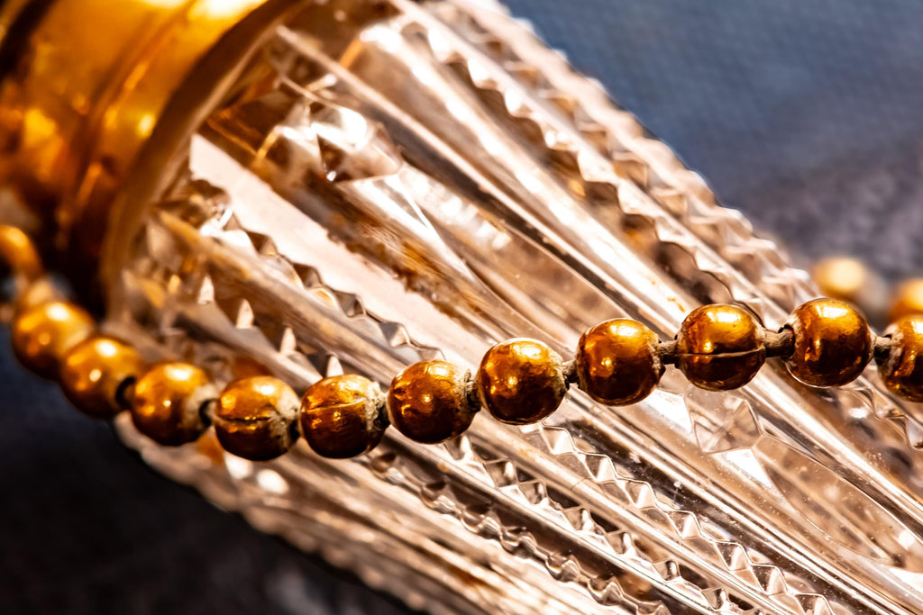 Close up of the chain of an Antique crystal horn-shaped perfume vial with brass detailing, attached to a chain and resting on a blue book.