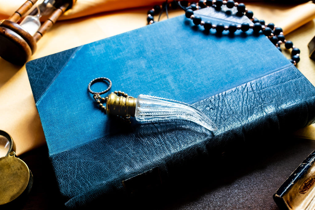 Antique crystal horn-shaped perfume vial with brass detailing, attached to a chain and resting on a blue book.