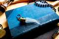 Antique crystal horn-shaped perfume vial with brass detailing, attached to a chain and resting on a blue book.