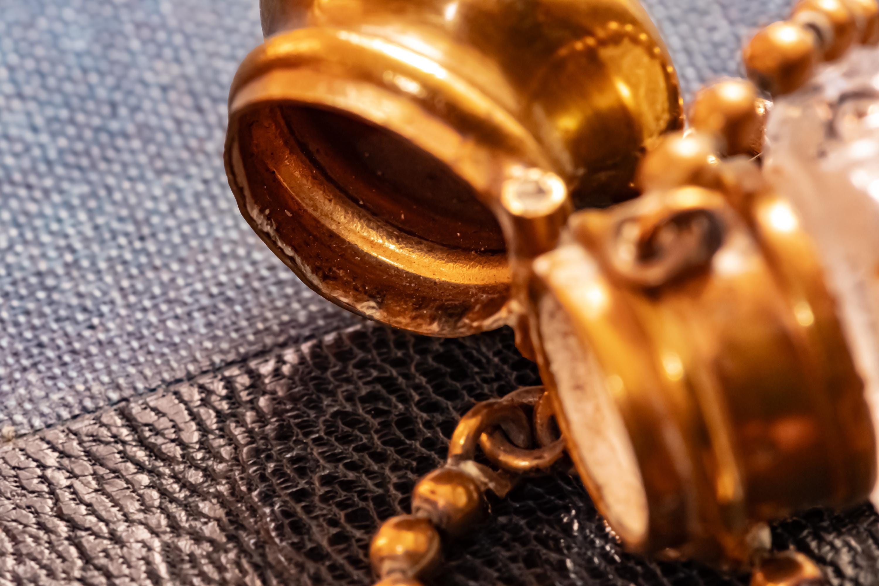 Close up of the open top of an Antique crystal horn-shaped perfume vial with brass detailing, attached to a chain and resting on a blue book.