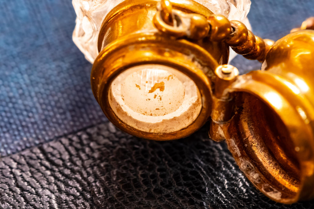 Close up of the top and inside of an Antique crystal horn-shaped perfume vial with brass detailing, attached to a chain and resting on a blue book.