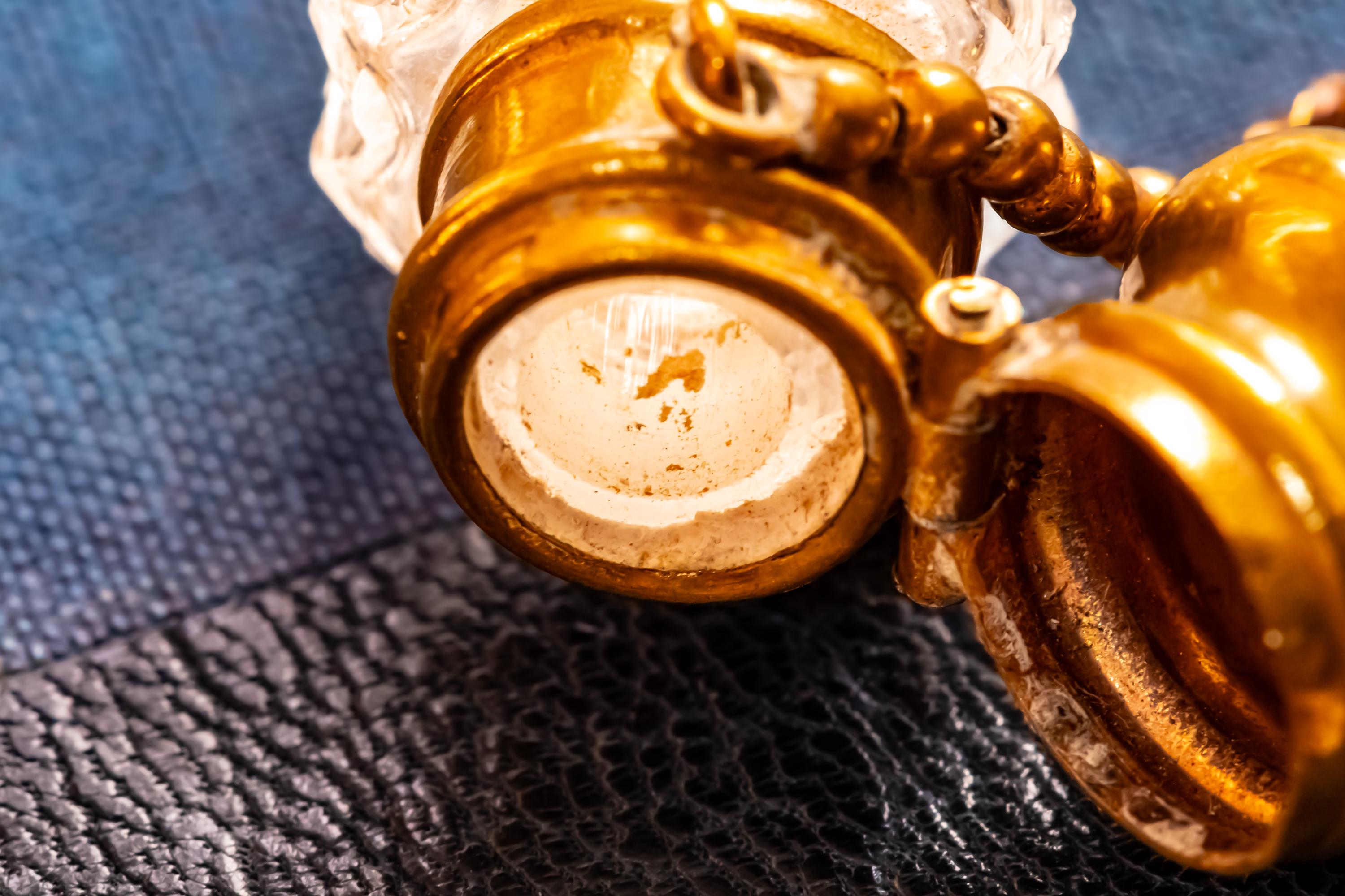 Close up of the top and inside of an Antique crystal horn-shaped perfume vial with brass detailing, attached to a chain and resting on a blue book.