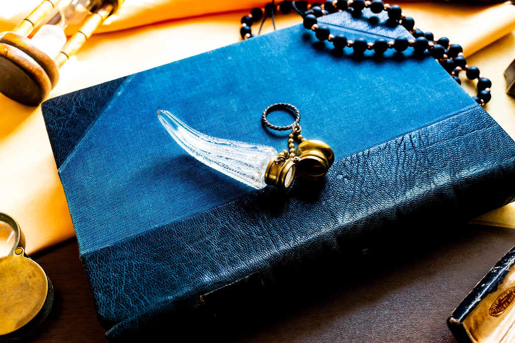 Antique crystal horn-shaped perfume vial with brass detailing, attached to a chain and resting on a blue book.