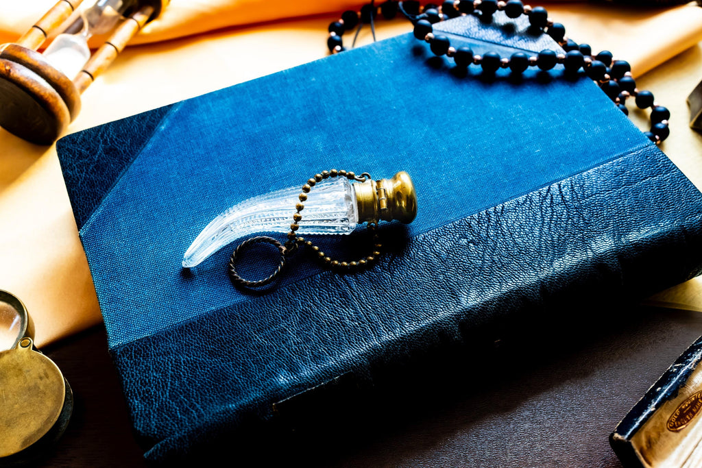 Antique crystal horn-shaped perfume vial with brass detailing, attached to a chain and resting on a blue book.