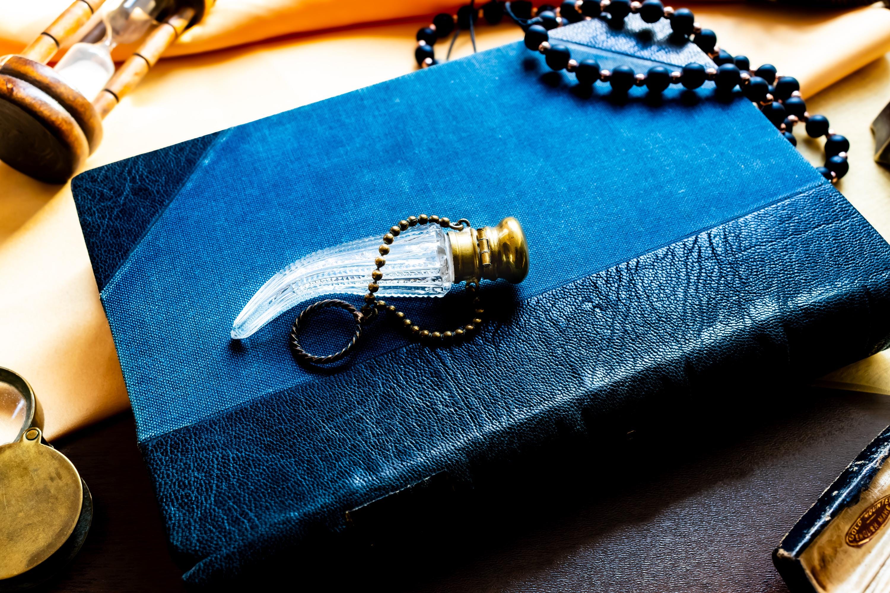 Antique crystal horn-shaped perfume vial with brass detailing, attached to a chain and resting on a blue book.