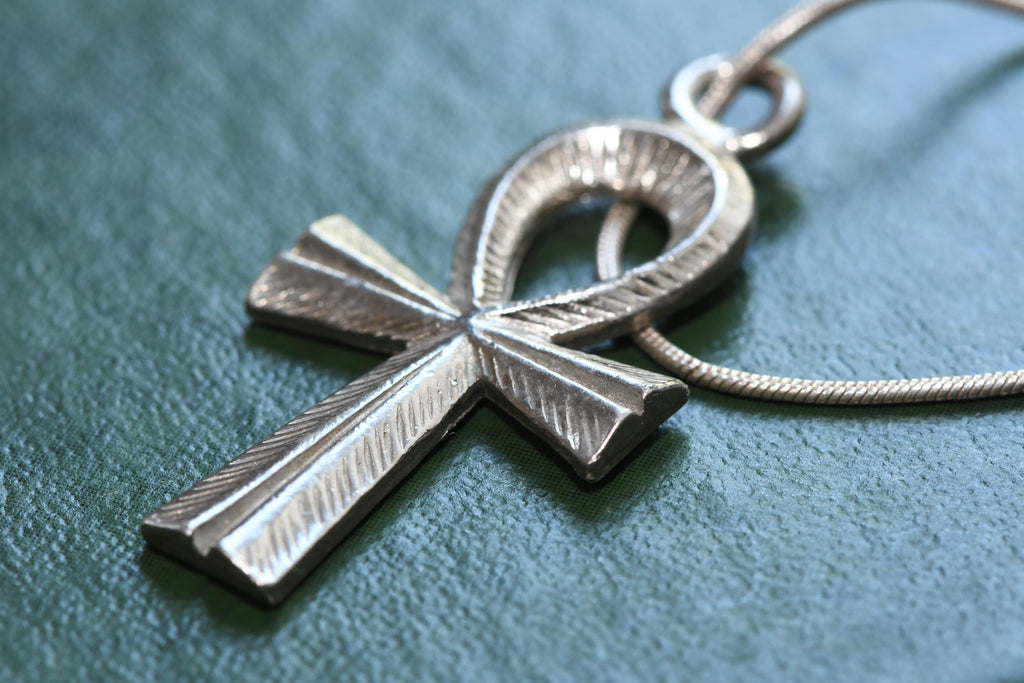 Textured sterling silver Ankh Egyptian cross pendant suspended on a fluid vintage silver snake chain. The everyday armor gothic jewelry rests on a dark green grimoire book.