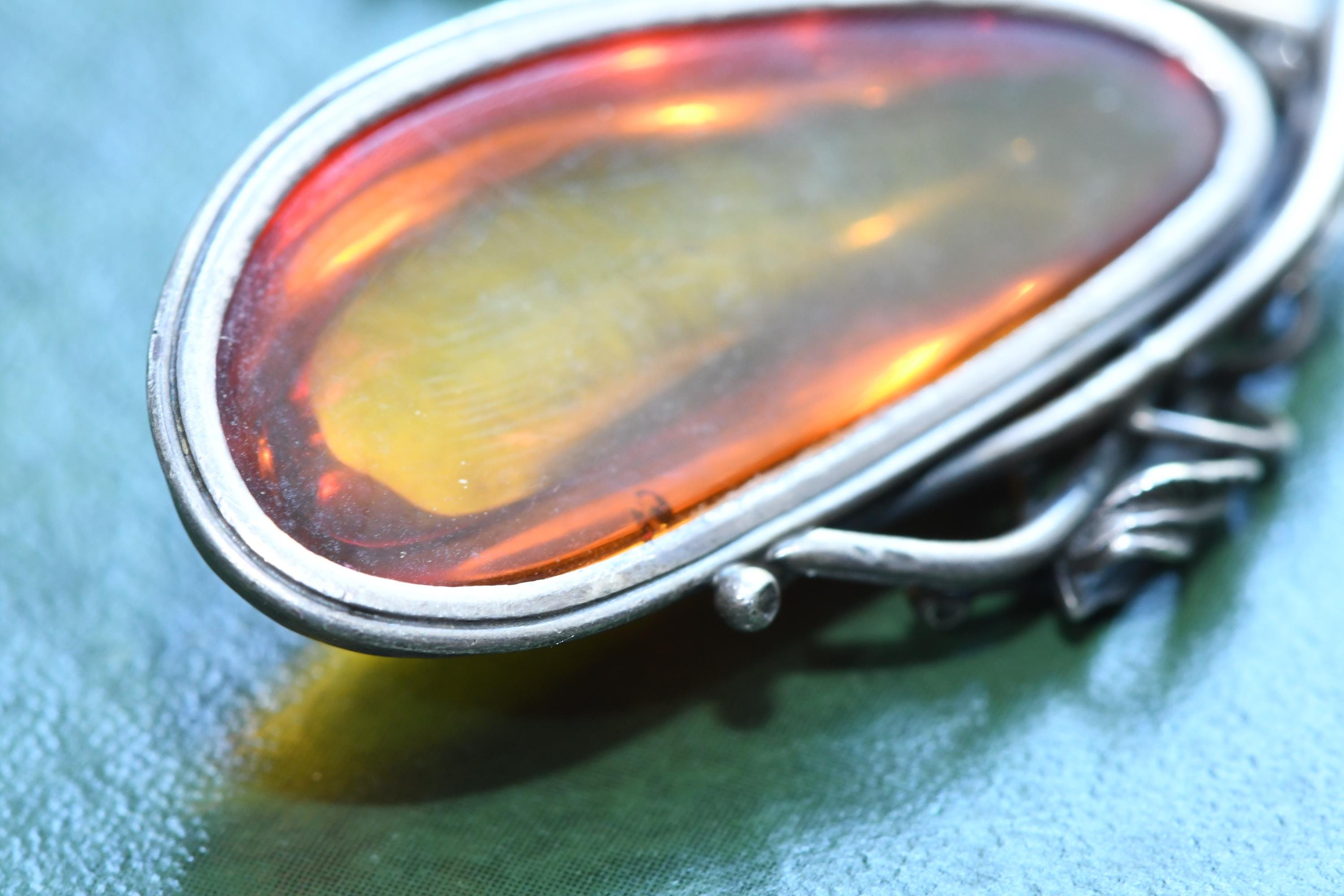 Large teardrop genuine Baltic amber pendant set in an oxidized sterling silver botanical leaf design. The brown witchy gothic necklace rests on a vintage green book alongside dark academia antiquities.