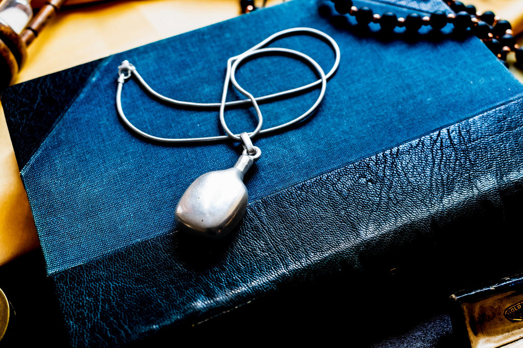 Heavy, smooth polished sterling silver antique potion flask pendant on a silver chain. The interactive Victorian scent bottle features a threaded cap and rests on a dark blue vintage book.