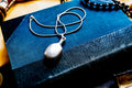 Heavy, smooth polished sterling silver antique potion flask pendant on a silver chain. The interactive Victorian scent bottle features a threaded cap and rests on a dark blue vintage book.