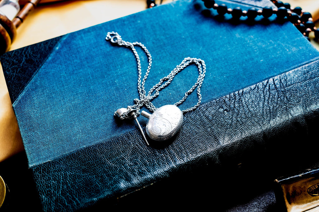 Miniature Victorian sterling silver perfume vial necklace. The antique poison bottle pendant features intricate botanical engravings and an unscrewed threaded cap with the original silver dauber wand attached