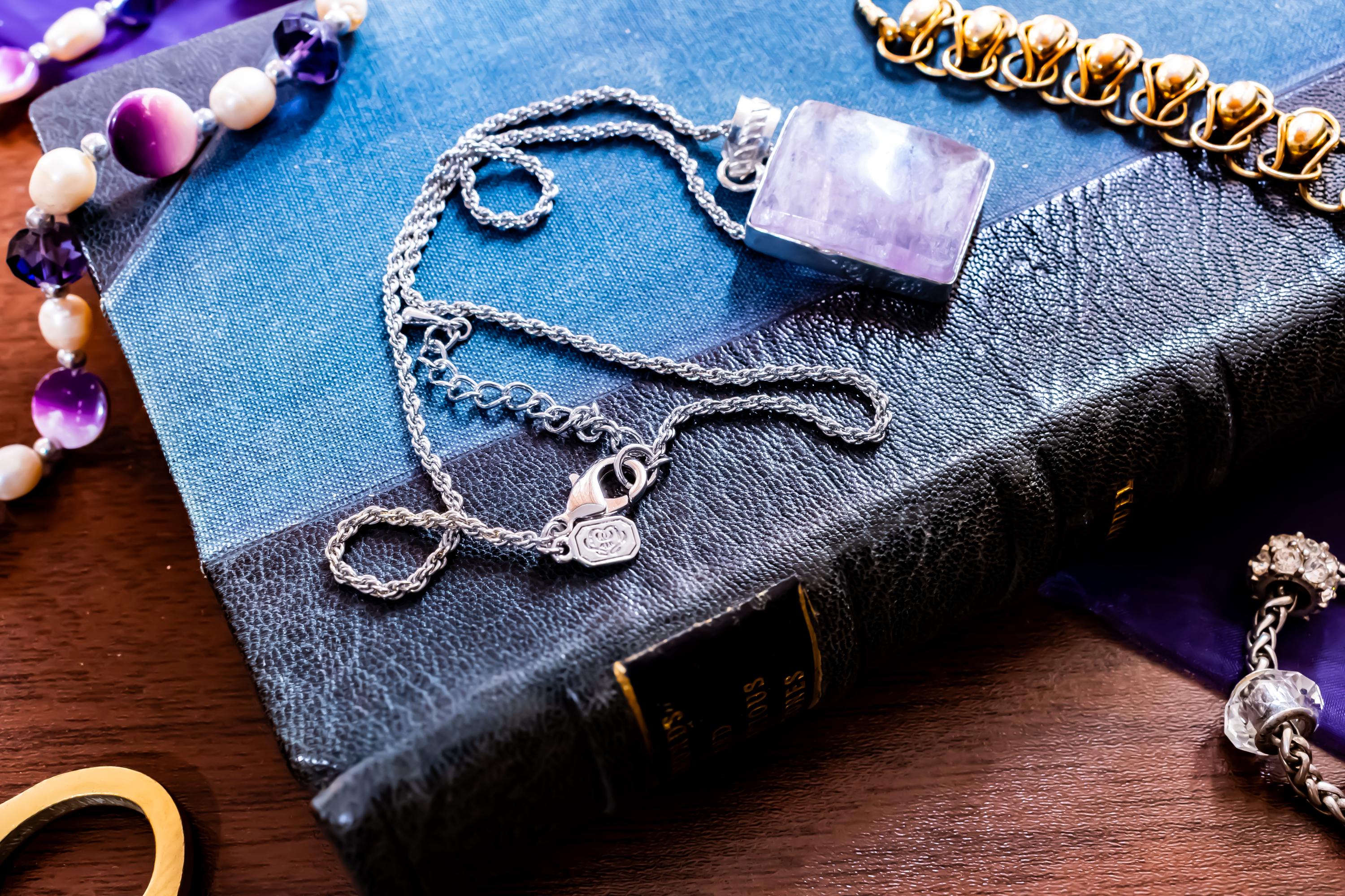 Close-up of a large, rectangular Kunzite gemstone pendant with natural pink and violet banding, set in 925 sterling silver and resting on a textured blue book.