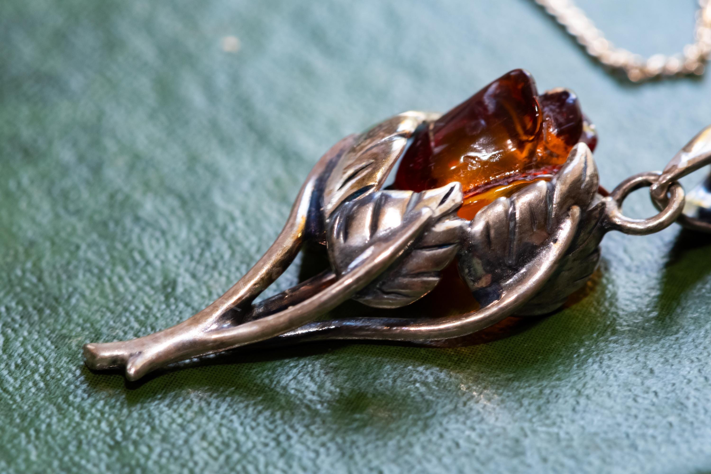 A vintage 925 sterling silver necklace featuring a carved Baltic amber rose pendant, beautifully staged resting on the cover of an antique green book with a dark carved brooch in the background.