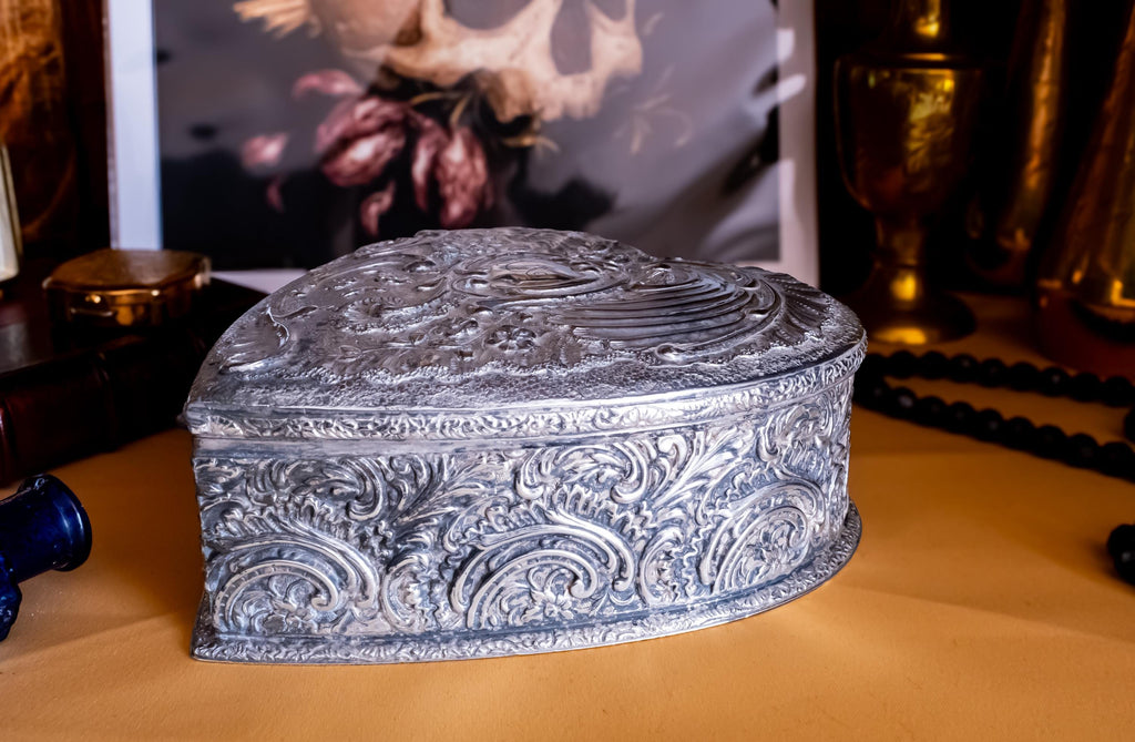 A solid sterling silver hand engraved jewelry box showing the engravings on one side. The shape of the jewelry box is a hard. It has engravings on the top and on the sides.