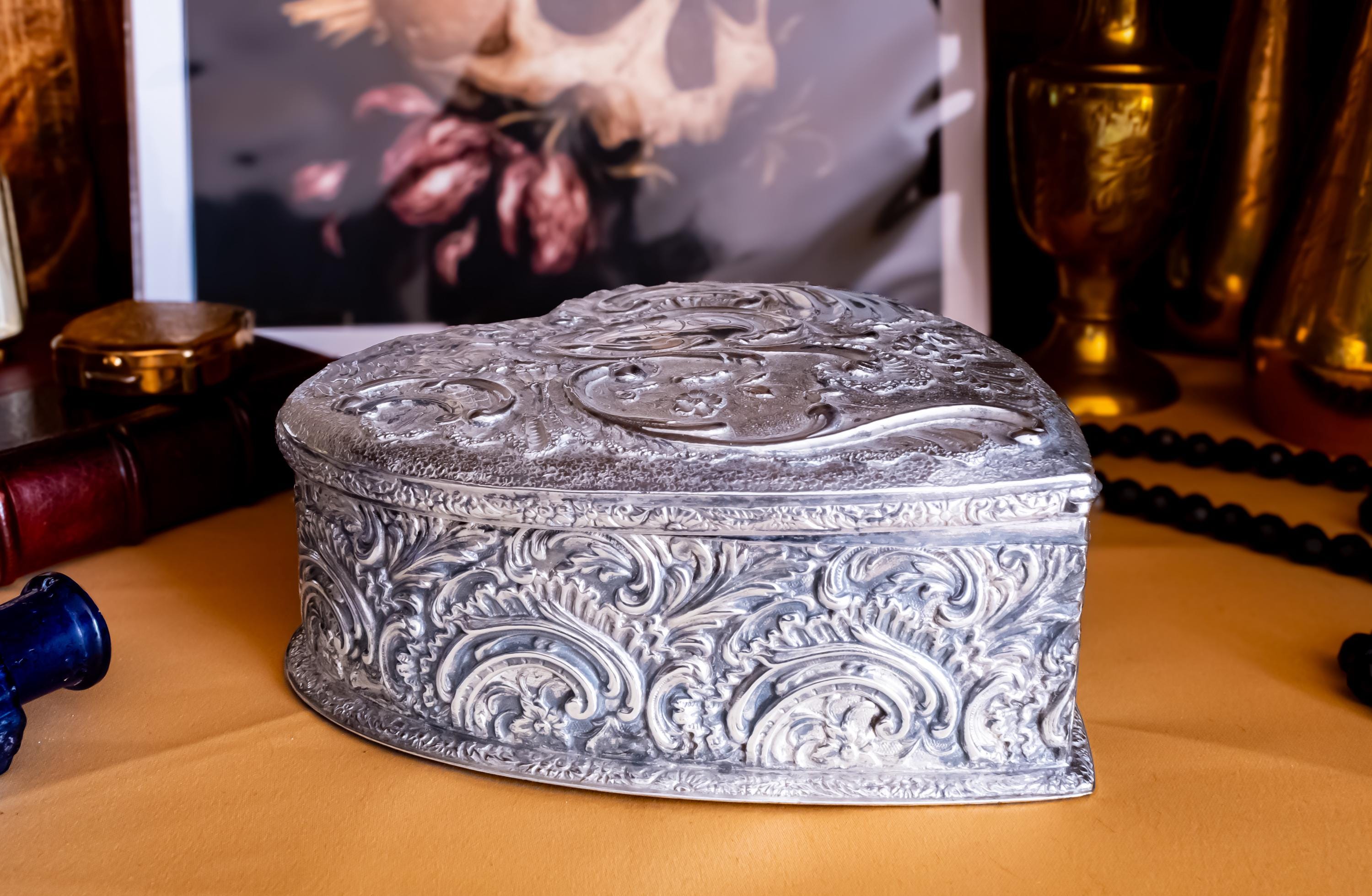A solid sterling silver hand engraved jewelry box showing the engravings on one side. The shape of the jewelry box is a hard. It has engravings on the top and on the sides.