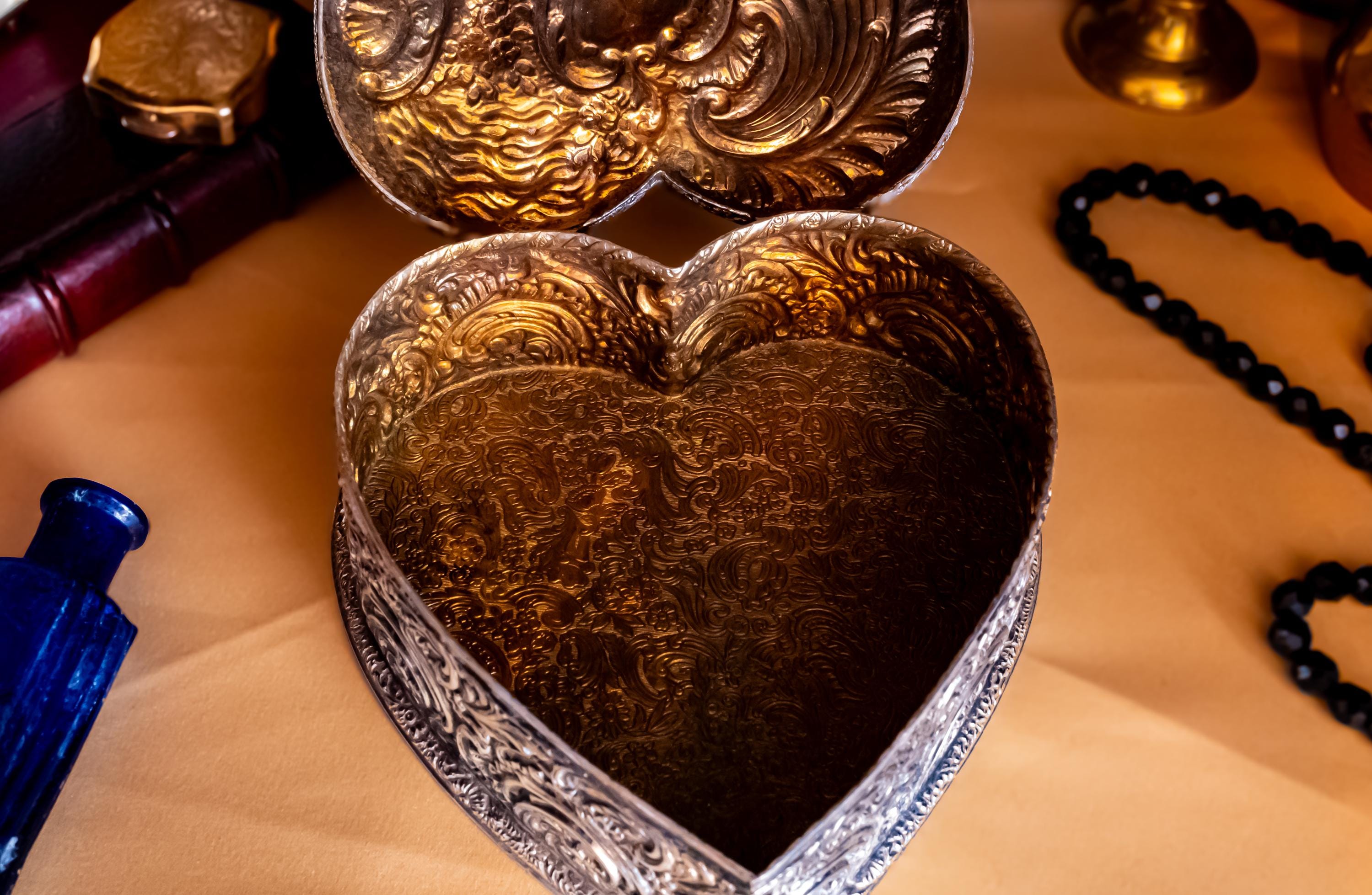 A solid sterling silver hand engraved jewelry box open to show the gold coloring of the inside. The shape of the jewelry box is a hard. It has engravings on the top and on the sides.