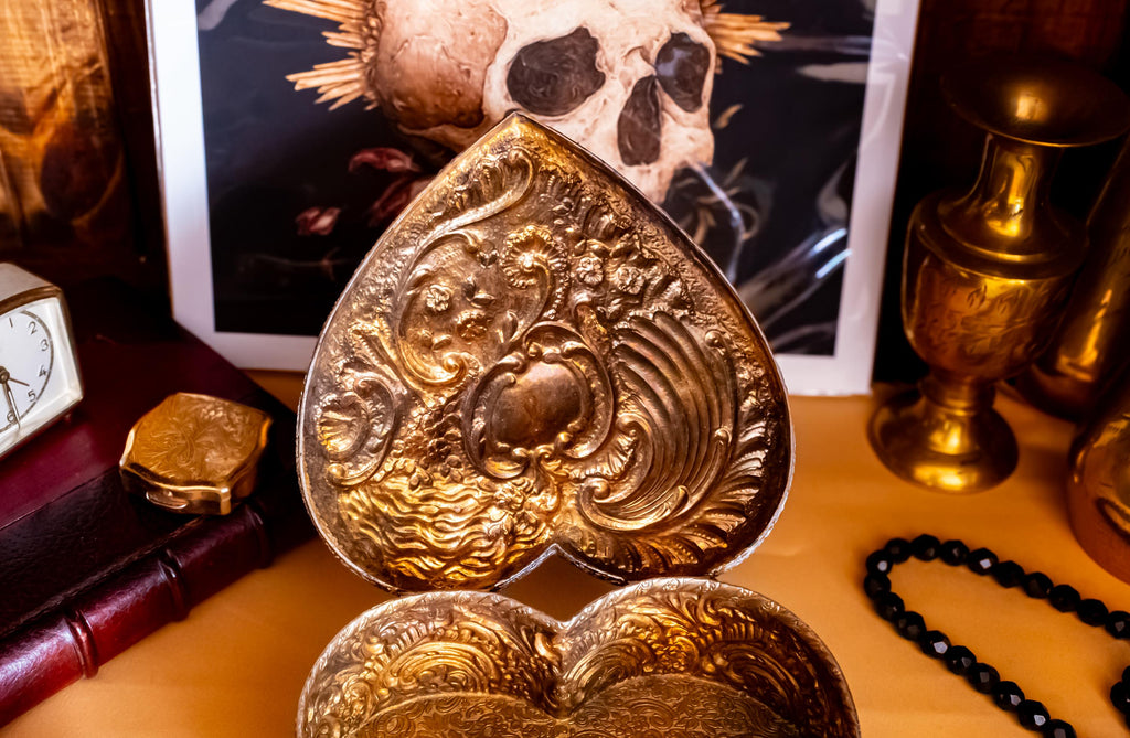 A solid sterling silver hand engraved jewelry box open to show the gold coloring of the inside. The shape of the jewelry box is a hard. It has engravings on the top and on the sides.