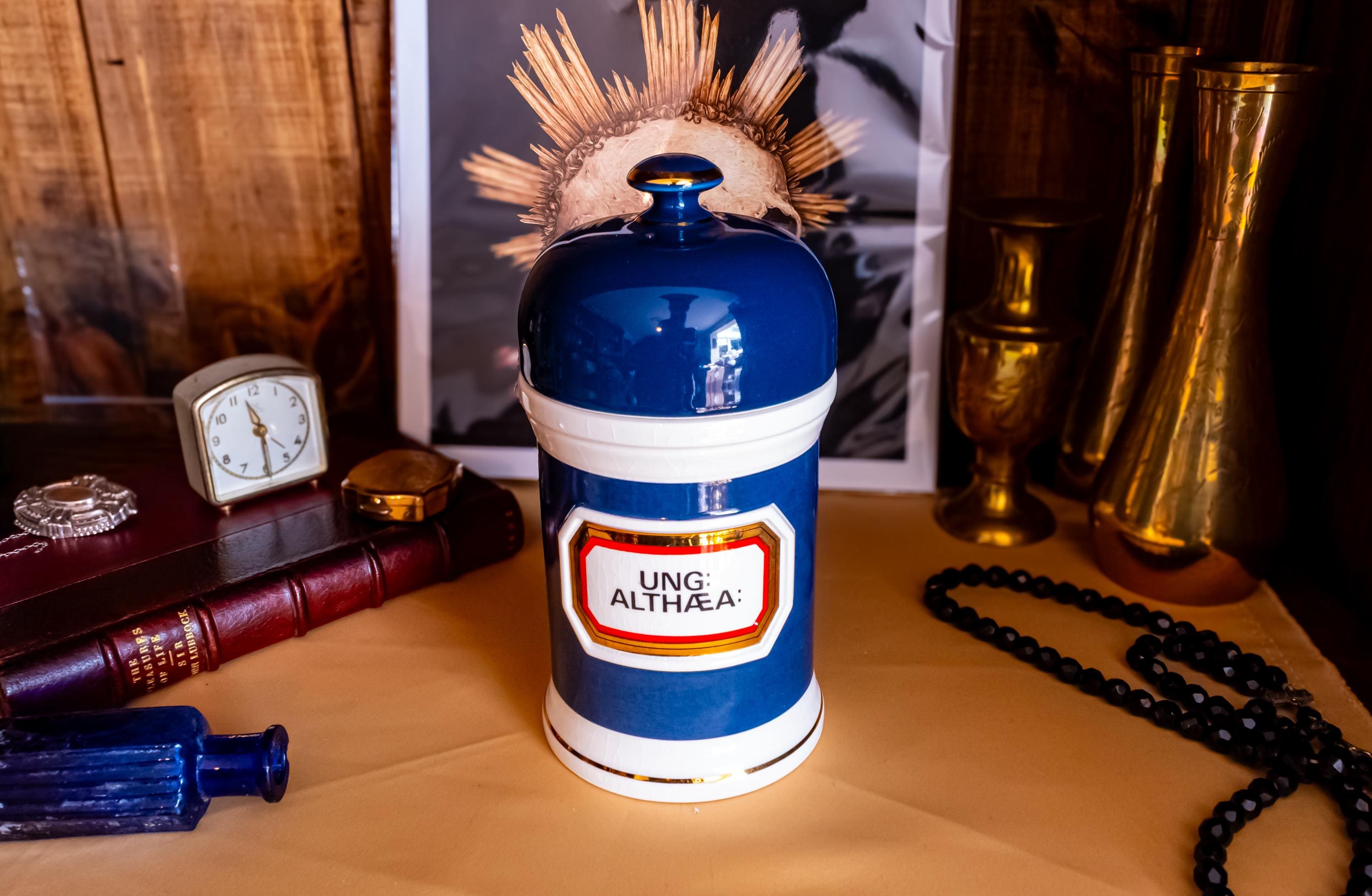 Antique apothecary blue and white jar with a label that says Ung: Althaea. The label is surrounded by gold foil. The white jar has a blue porcelain lid.