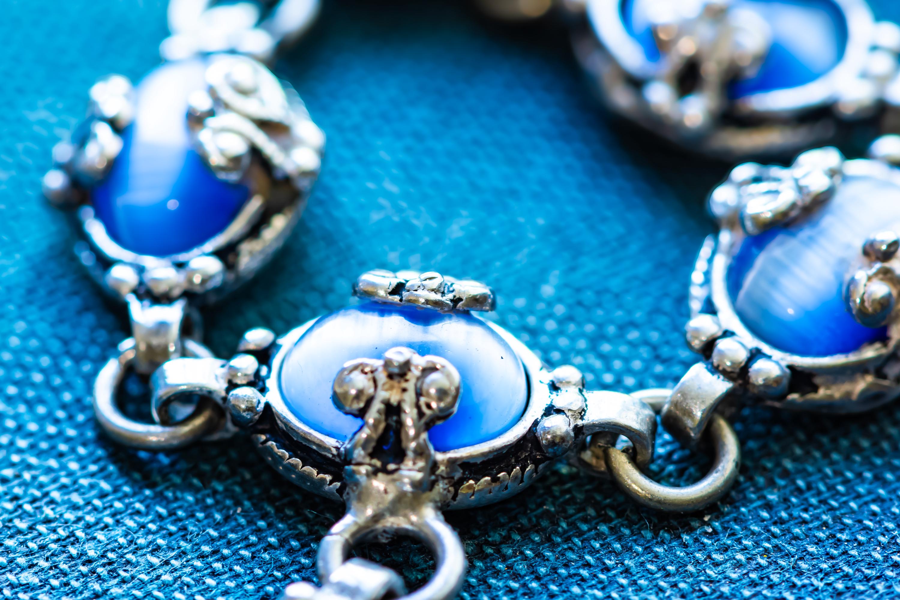 A vintage 925 sterling silver necklace featuring ornate links set with glowing blue cat's eye cabochons in a Y-drop design, resting beautifully on a textured teal book.