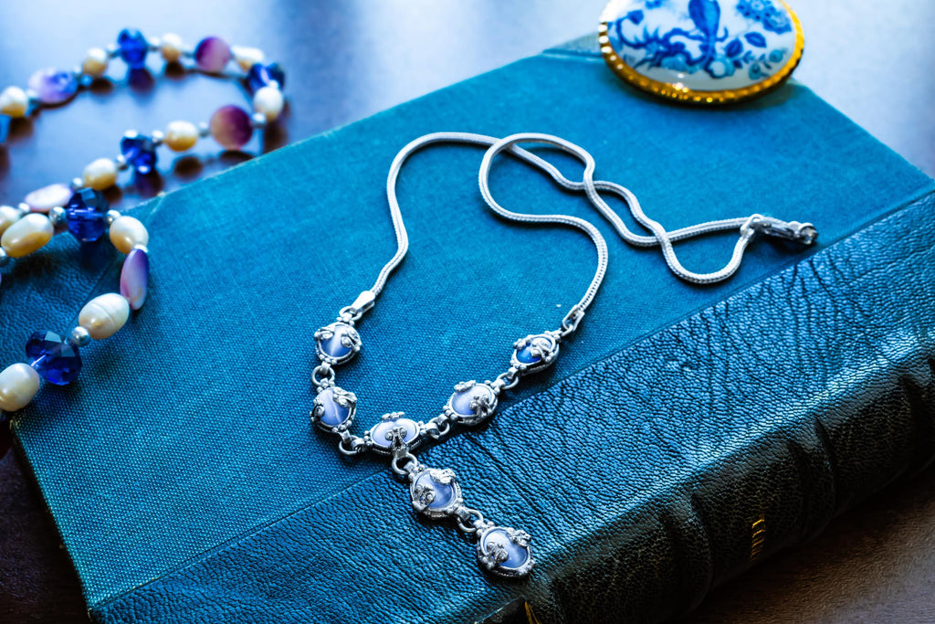 A vintage 925 sterling silver necklace featuring ornate links set with glowing blue cat's eye cabochons in a Y-drop design, resting beautifully on a textured teal book.