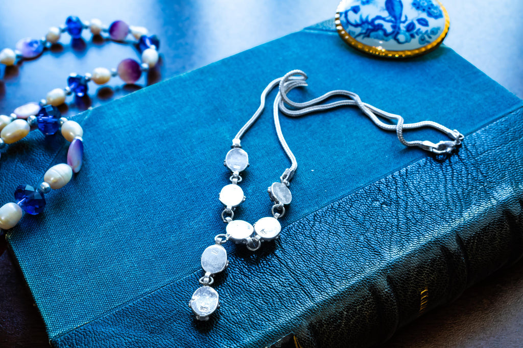 A vintage 925 sterling silver necklace featuring ornate links set with glowing blue cat's eye cabochons in a Y-drop design, resting beautifully on a textured teal book.