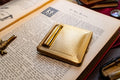 A gleaming gold vintage Kigu of London rectangular compact with a basketweave pattern and integrated lipstick holder, resting on an open antique book.