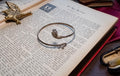 vintage 925 sterling silver bypass bangle featuring two sculpted serpent heads, resting beautifully on the text of an open antique book.
