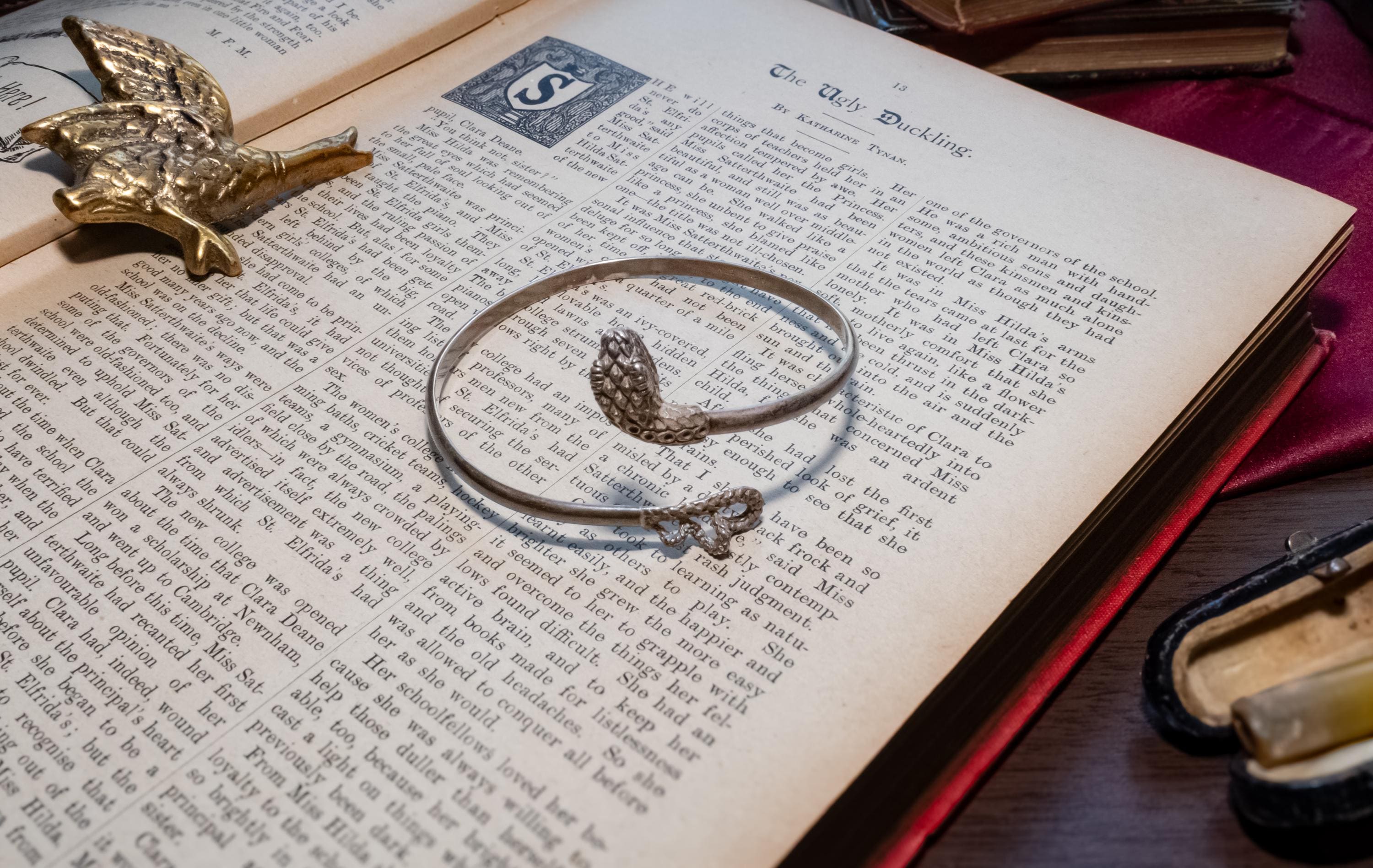 vintage 925 sterling silver bypass bangle featuring two sculpted serpent heads, resting beautifully on the text of an open antique book.