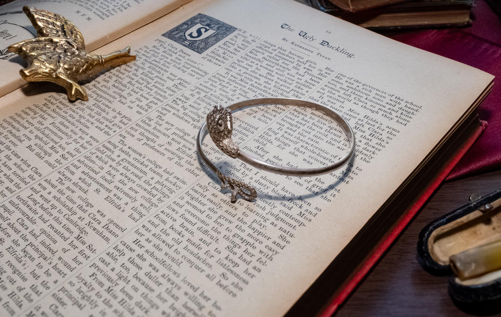 vintage 925 sterling silver bypass bangle featuring two sculpted serpent heads, resting beautifully on the text of an open antique book.
