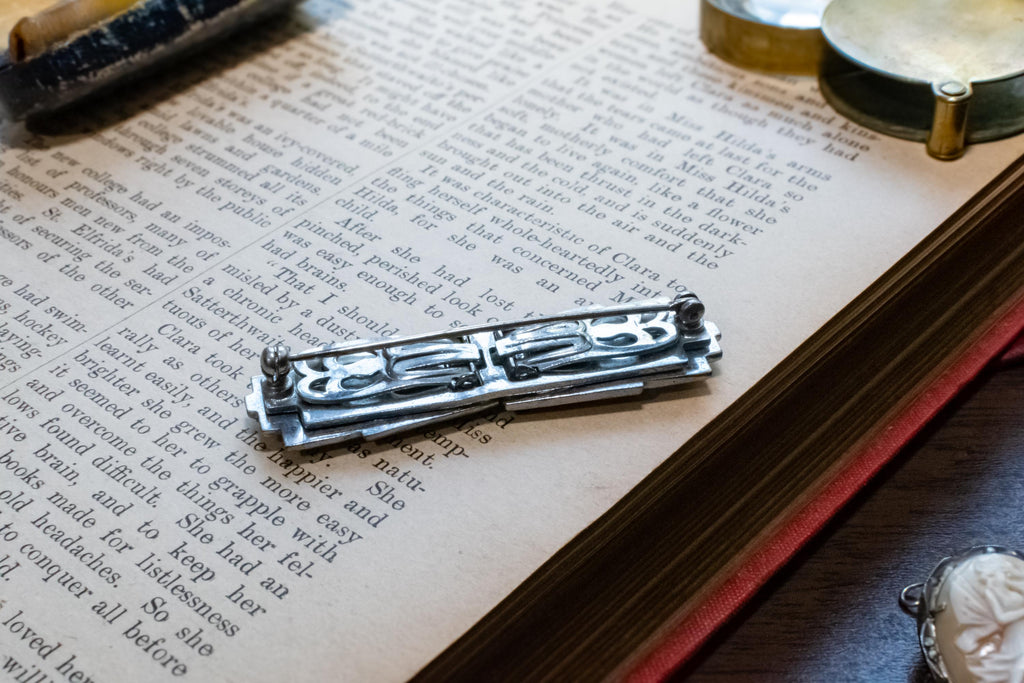 A silver-toned metal brooch, resting on an open vintage book with printed text.