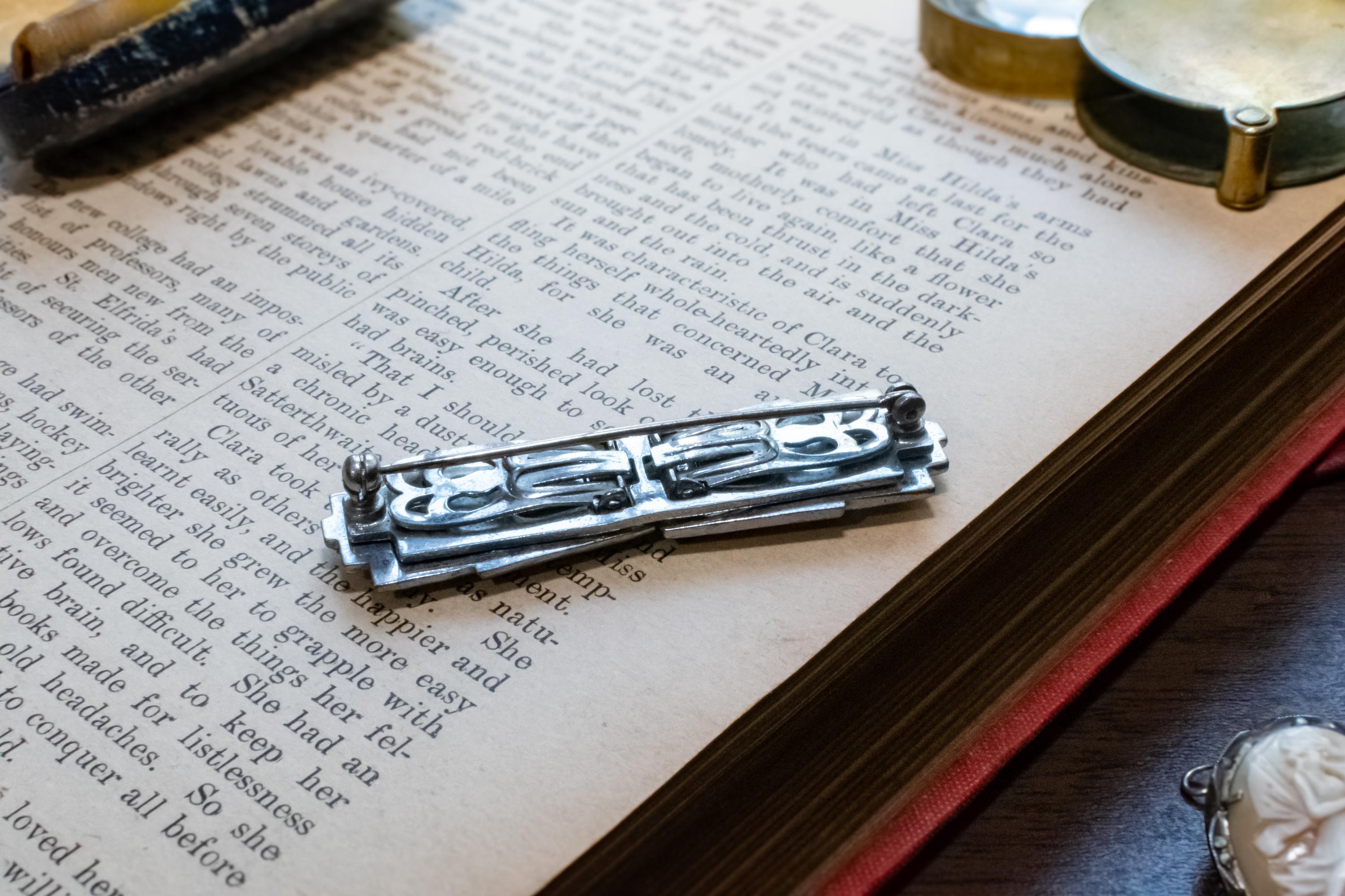A silver-toned metal brooch, resting on an open vintage book with printed text.