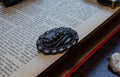 A dark carved brooch with a floral and leaf design, resting on the pages of an open vintage book.