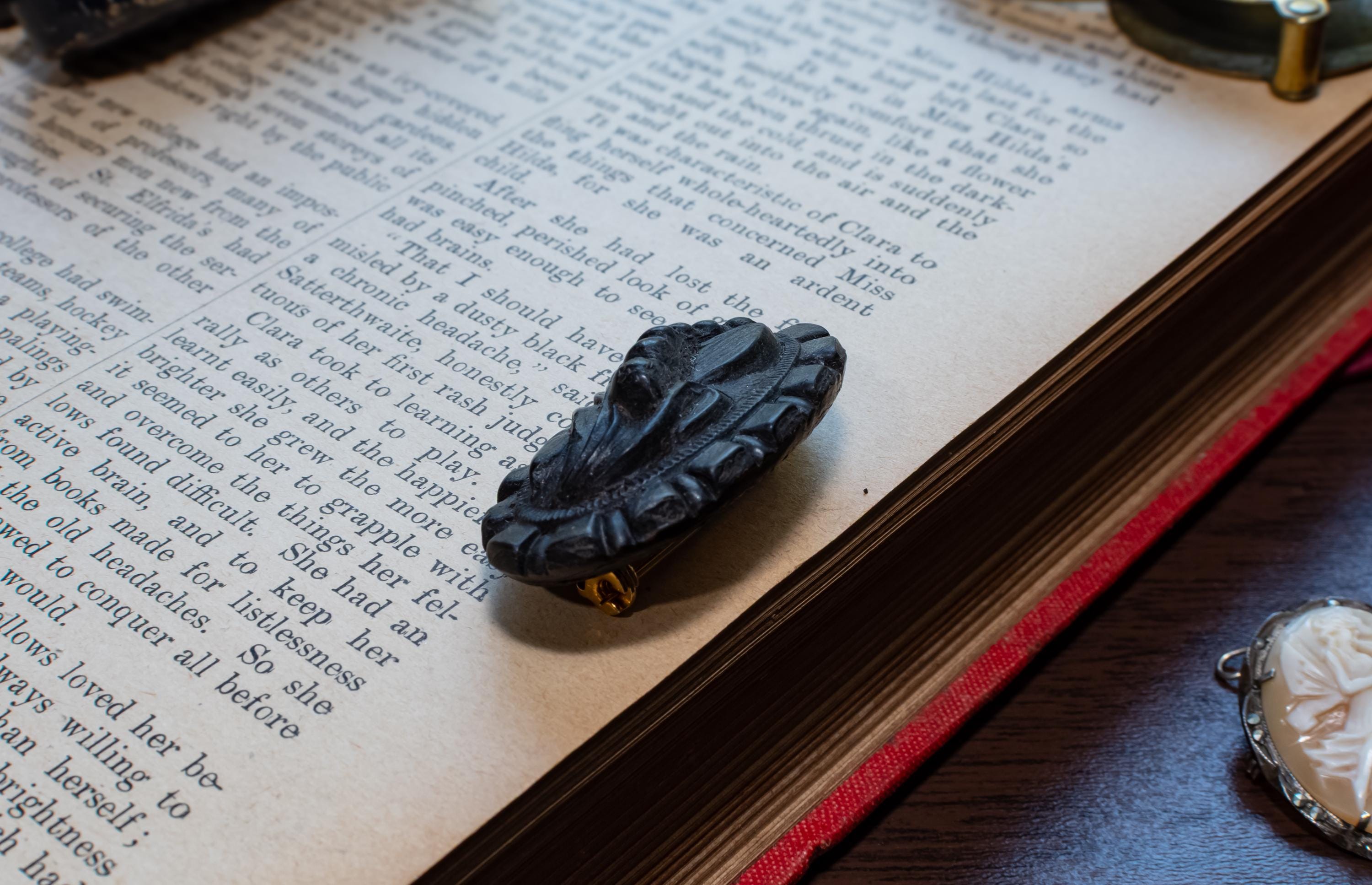 A carved black brooch with a gold-toned loop, resting on the pages of an open vintage book.