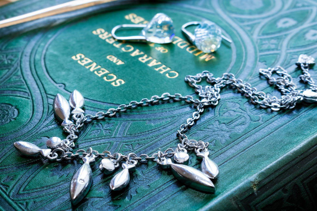 Vintage silver-tone Swarovski crystal necklace featuring round and marquise cut rhinestones, paired with matching crystal stud earrings, resting on a green antique book.