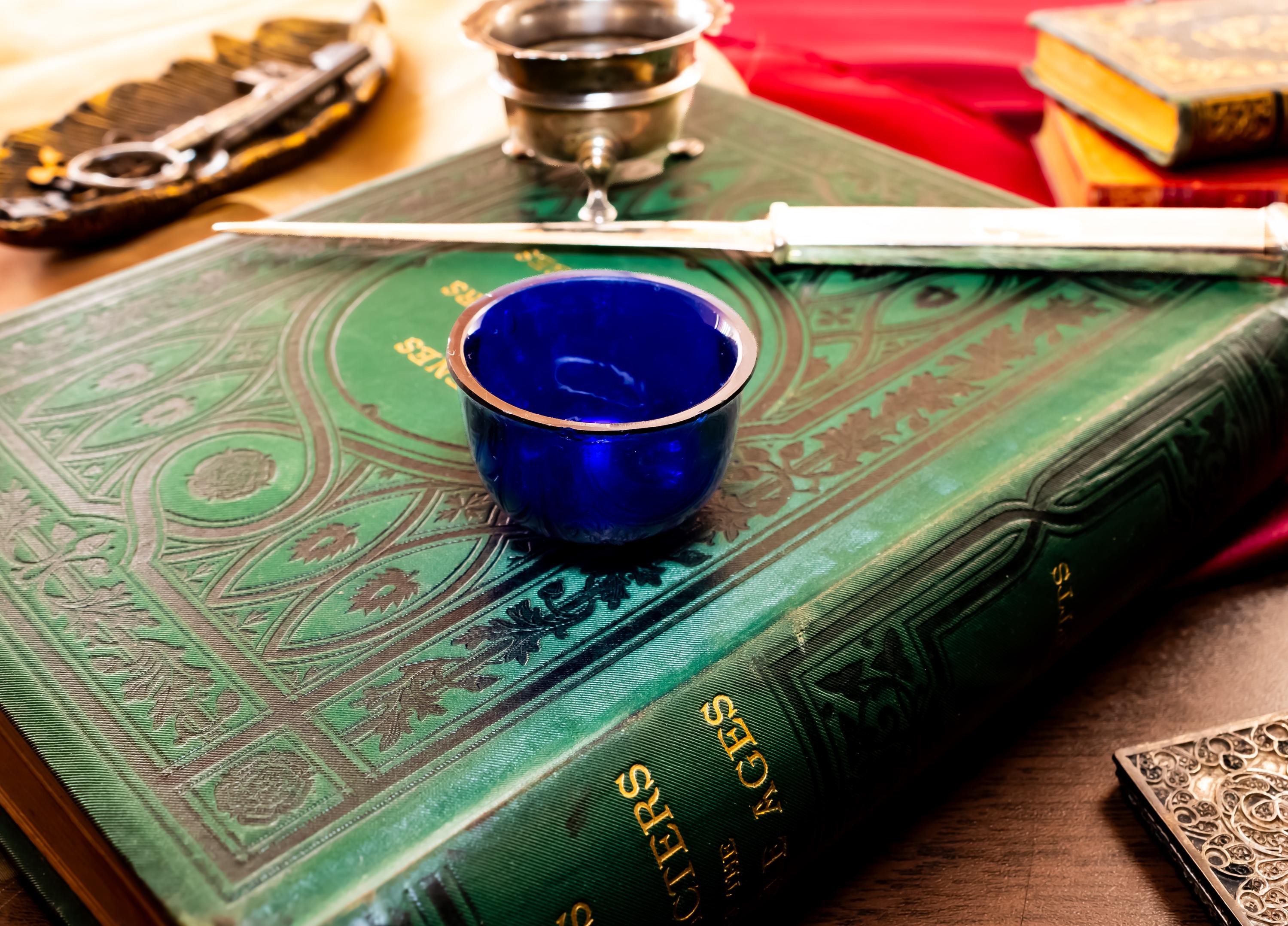 Image showing the cobalt blue liner of Antique footed silver master salt cellar, resting on top of an ornate green vintage book.