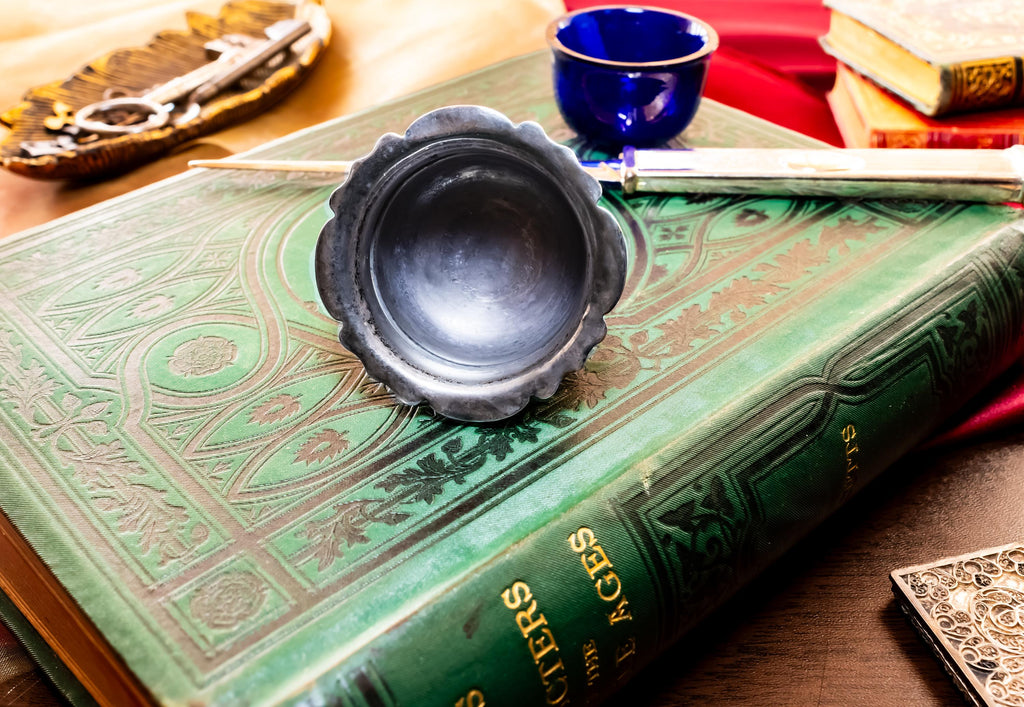 Image showing the inside of Antique footed silver master salt cellar containing a vibrant cobalt blue glass liner, resting on top of an ornate green vintage book.