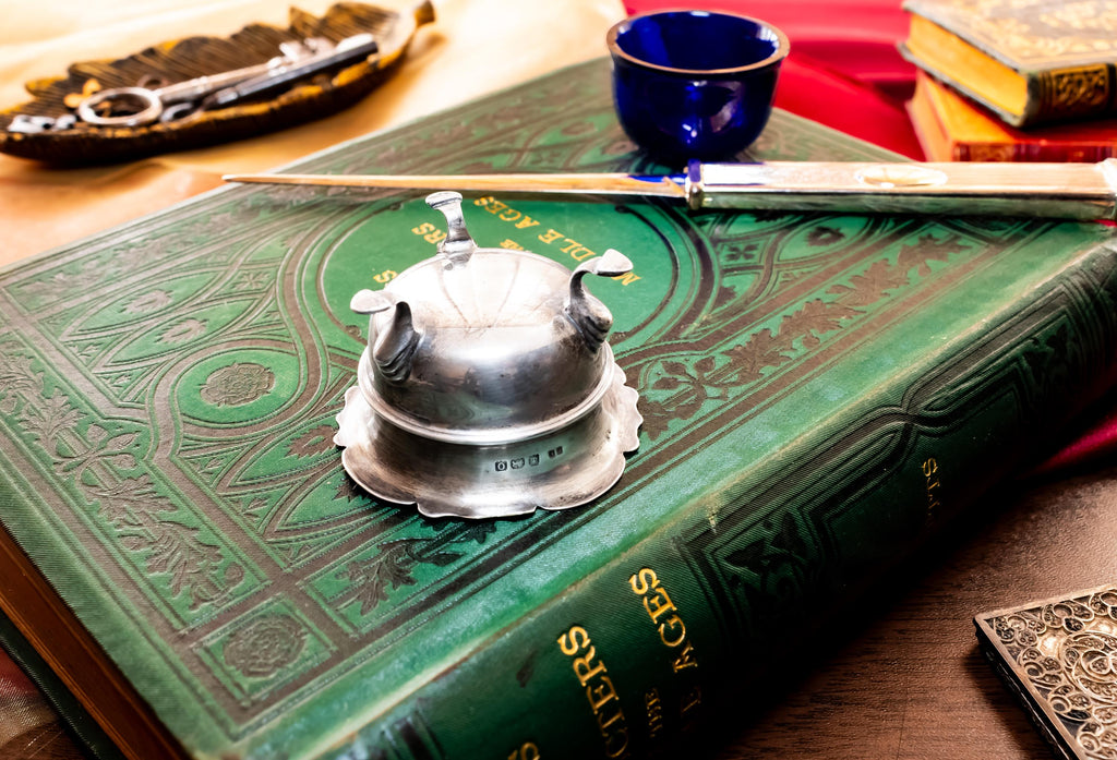 Image showing the bottom of Antique footed silver master salt cellar containing a vibrant cobalt blue glass liner, resting on top of an ornate green vintage book.