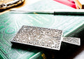 Antique rectangular silver hand mirror featuring intricate swirling filigree wirework on the back and a beveled glass front, resting on a green vintage book.