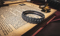 An antique 1883 heavy sterling silver cuff bracelet by Robert James Dick featuring intricate geometric and beadwork detailing, resting on the text of an open vintage book.