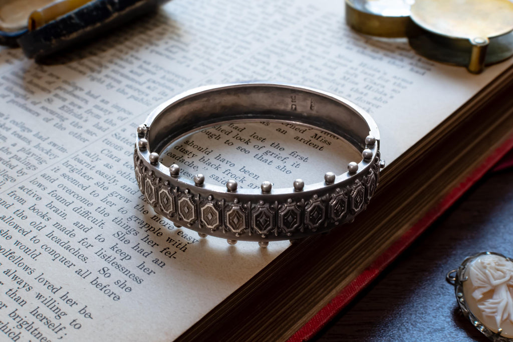 An antique 1883 heavy sterling silver cuff bracelet by Robert James Dick featuring intricate geometric and beadwork detailing, resting on the text of an open vintage book.