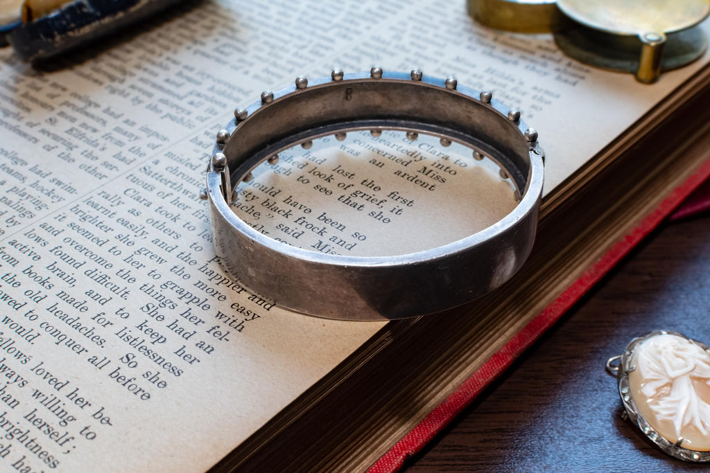An antique 1883 heavy sterling silver cuff bracelet by Robert James Dick featuring intricate geometric and beadwork detailing, resting on the text of an open vintage book.