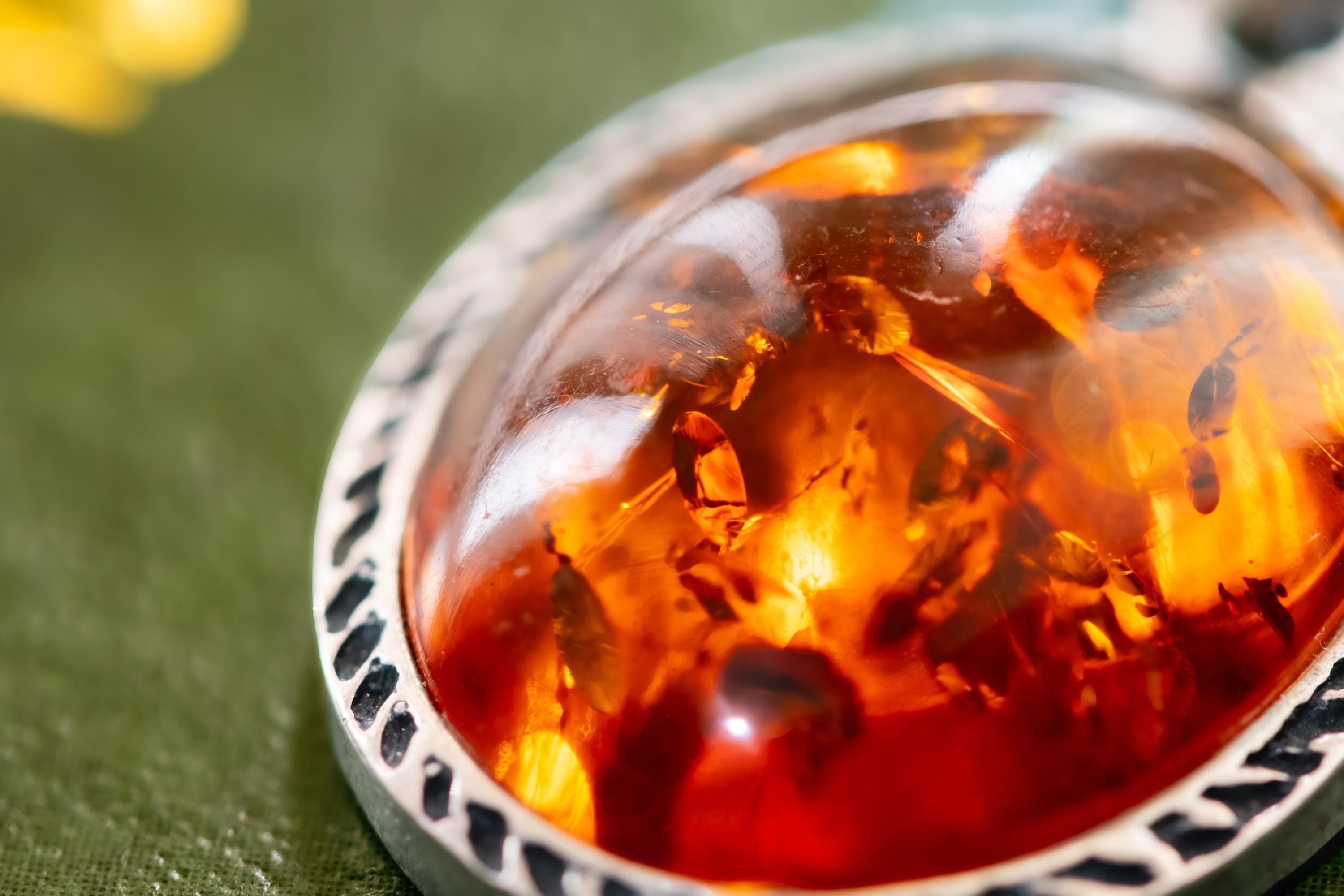 Close-up of a vintage 925 sterling silver necklace featuring a polished oval Baltic amber cabochon with a twisted silver rope border, resting on a dark green book with gold foil detailing