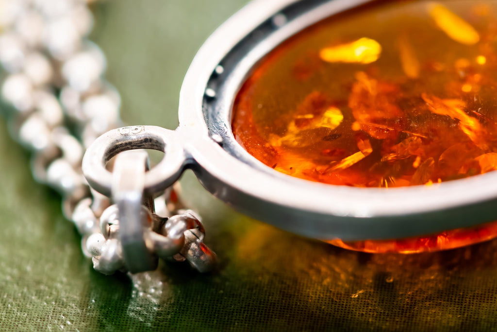 Close-up of a vintage 925 sterling silver necklace featuring a polished oval Baltic amber cabochon with a twisted silver rope border, resting on a dark green book with gold foil detailing