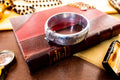 A wide vintage 1969 Birmingham sterling silver hinged bangle with intricate botanical engravings and a safety chain, resting beautifully on a vintage leather-bound book.
