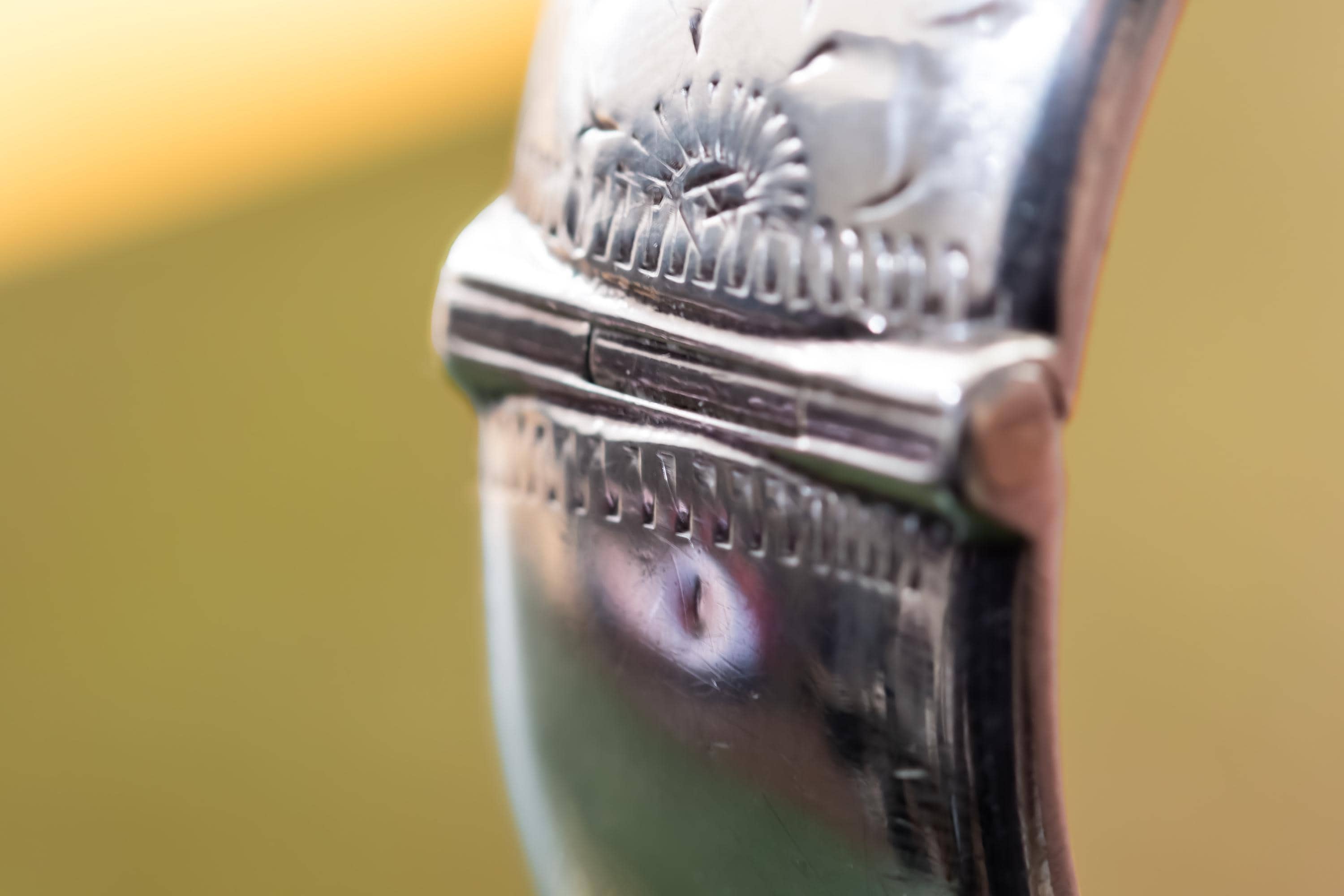 Close-up of a wide, vintage 1969 Birmingham sterling silver hinged bangle with intricate botanical engravings and a safety chain, resting beautifully on a vintage leather-bound book.
